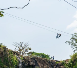 two unrecognizable people seen from afar descending canopy front waterfall 1