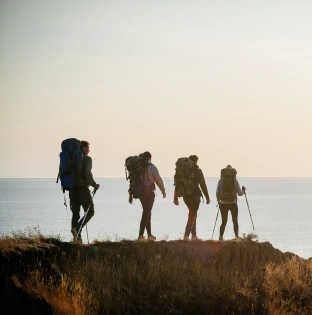 four travelers with backpacks walking mountain top near sea